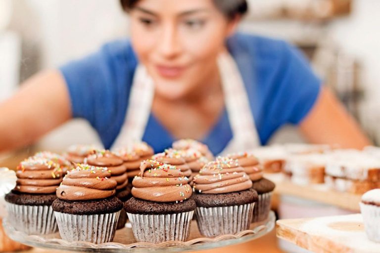 Eine Frau mit blauer Bluse dekoriert Schokoladen-Cupcakes in einem Café.